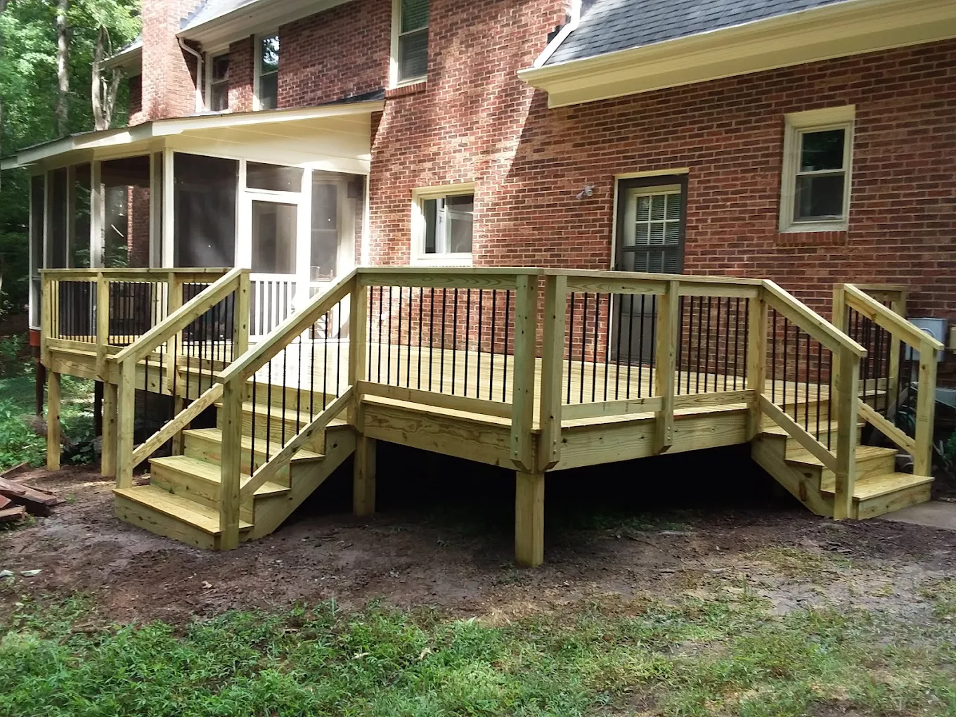 Newly built wraparound wood deck with black balusters and two staircases on a brick home